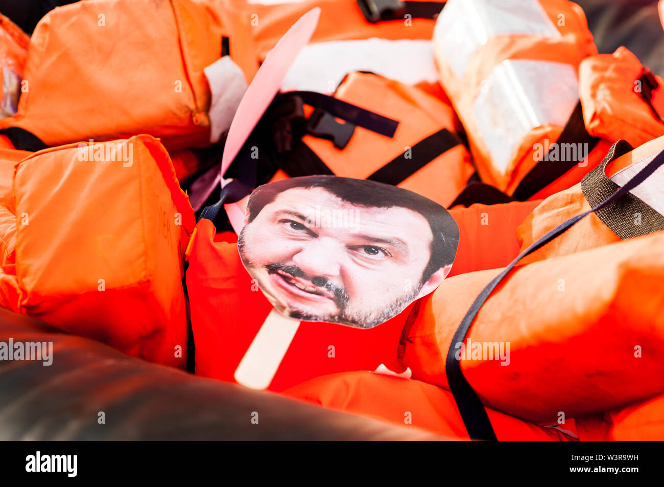 Barcelona, spain- 14 july 2019: mask of salvini face  drowning inside rubber dinghy with life belts and proactiva open arms stickers as a symbol of mi Stock Photo