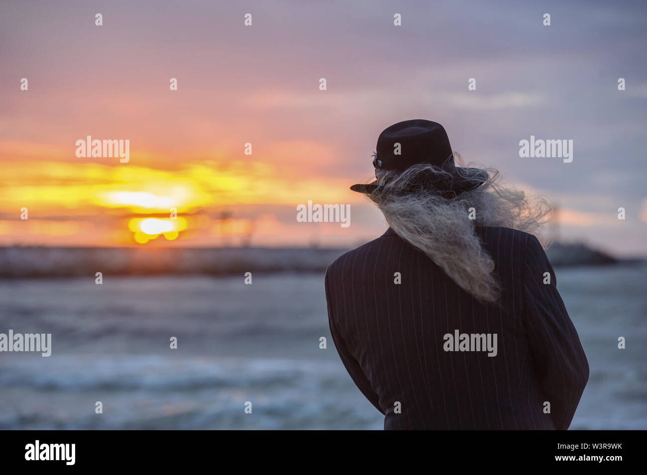 old man looking towards the sun setting over the sea Stock Photo