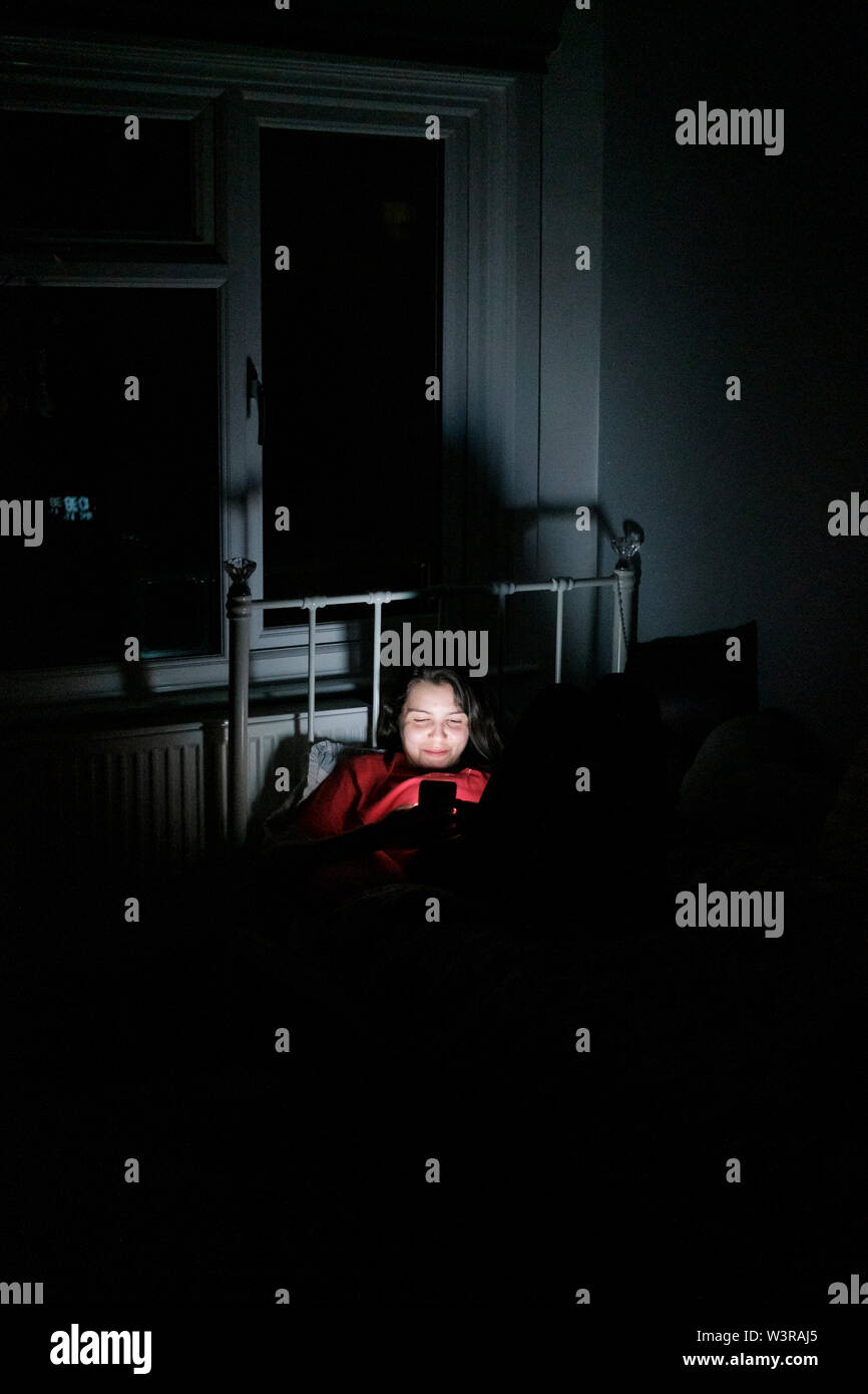 Teenage girl, 17 years old , looking at smartphone late at night in bed Stock Photo