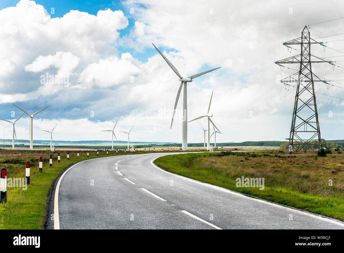 Country road through a wind turbins and high voltage pylons and cloudy sky Stock Photo
