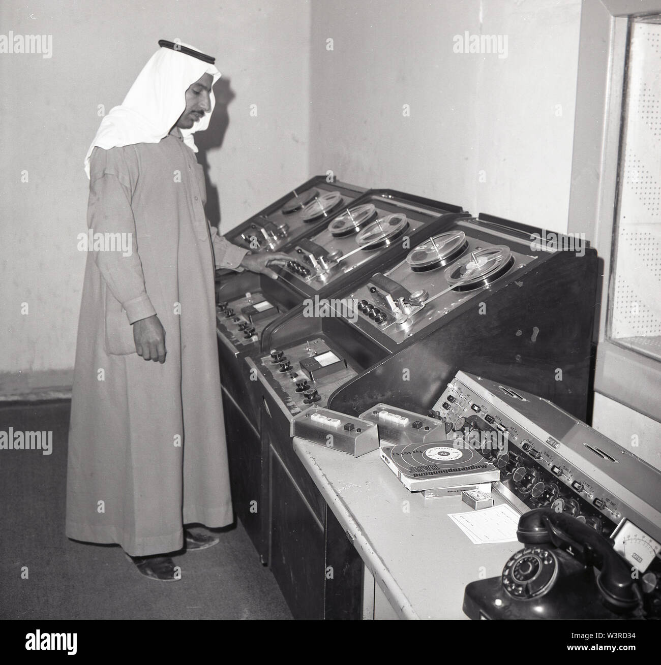 1960s, historical, an Arab studio technician wearing a traditional ankle-length garnent of an Thawb or Thobe and headdress, a Keffiyeh, working at a tape machine in a television broadcast facility, Saudia Arabia. Stock Photo