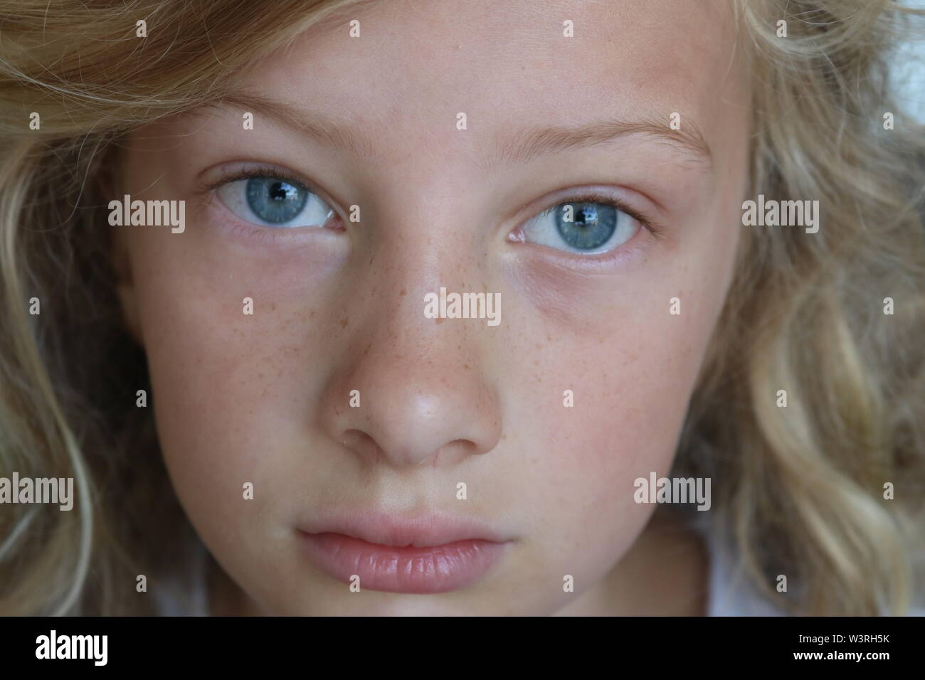 Closeup of a beautiful preteen girl with blue eyes and a sad, serious stare Stock Photo