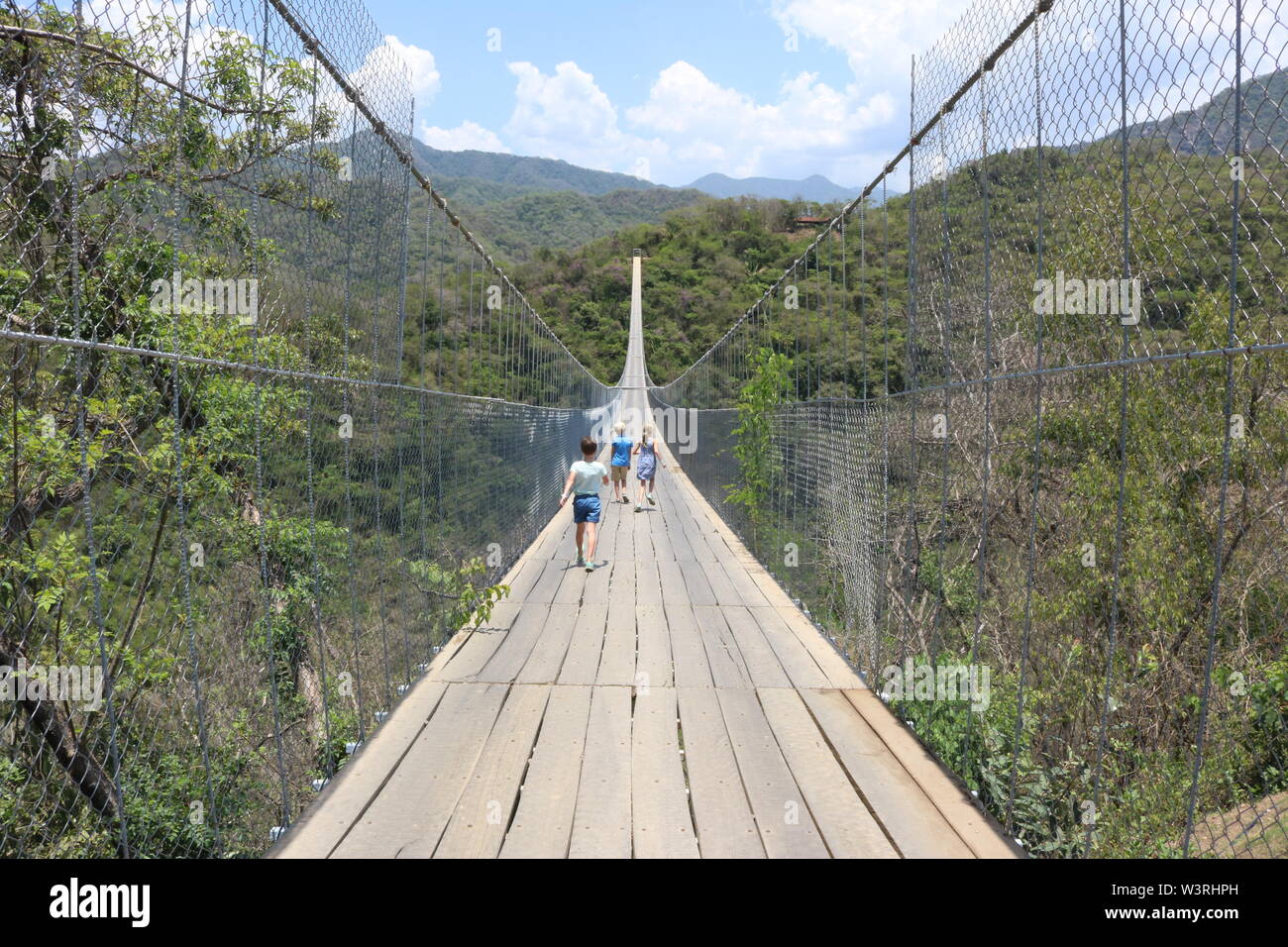 Three children walking on a long suspension bridge in the jungle in Puerto Vallarta, Mexico Stock Photo