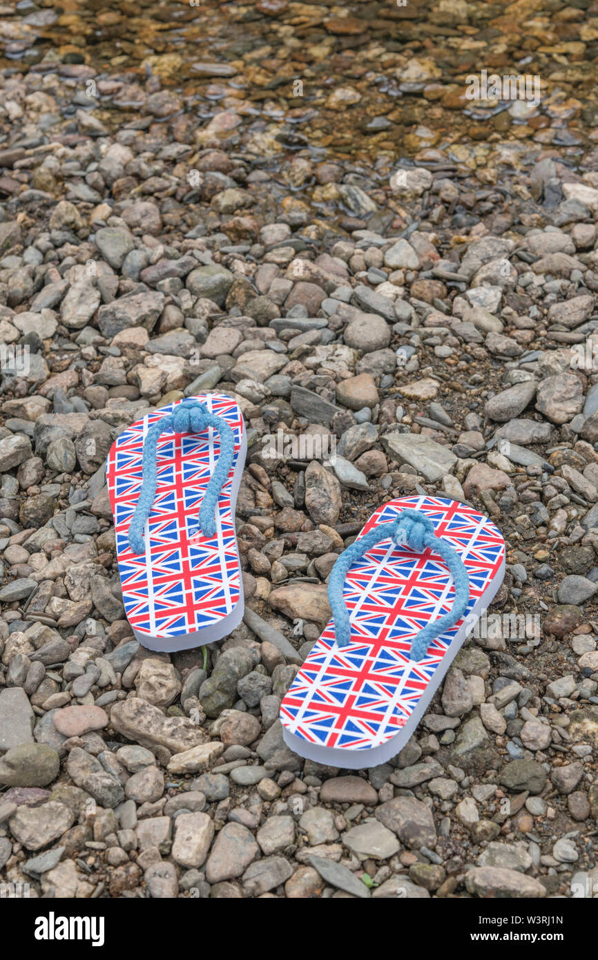 GB flag / Union Jack flip-flops on river shingle - for 2021 UK staycation, holidays at home, staycation Cornwall, country break, flip-flop footwear. Stock Photo