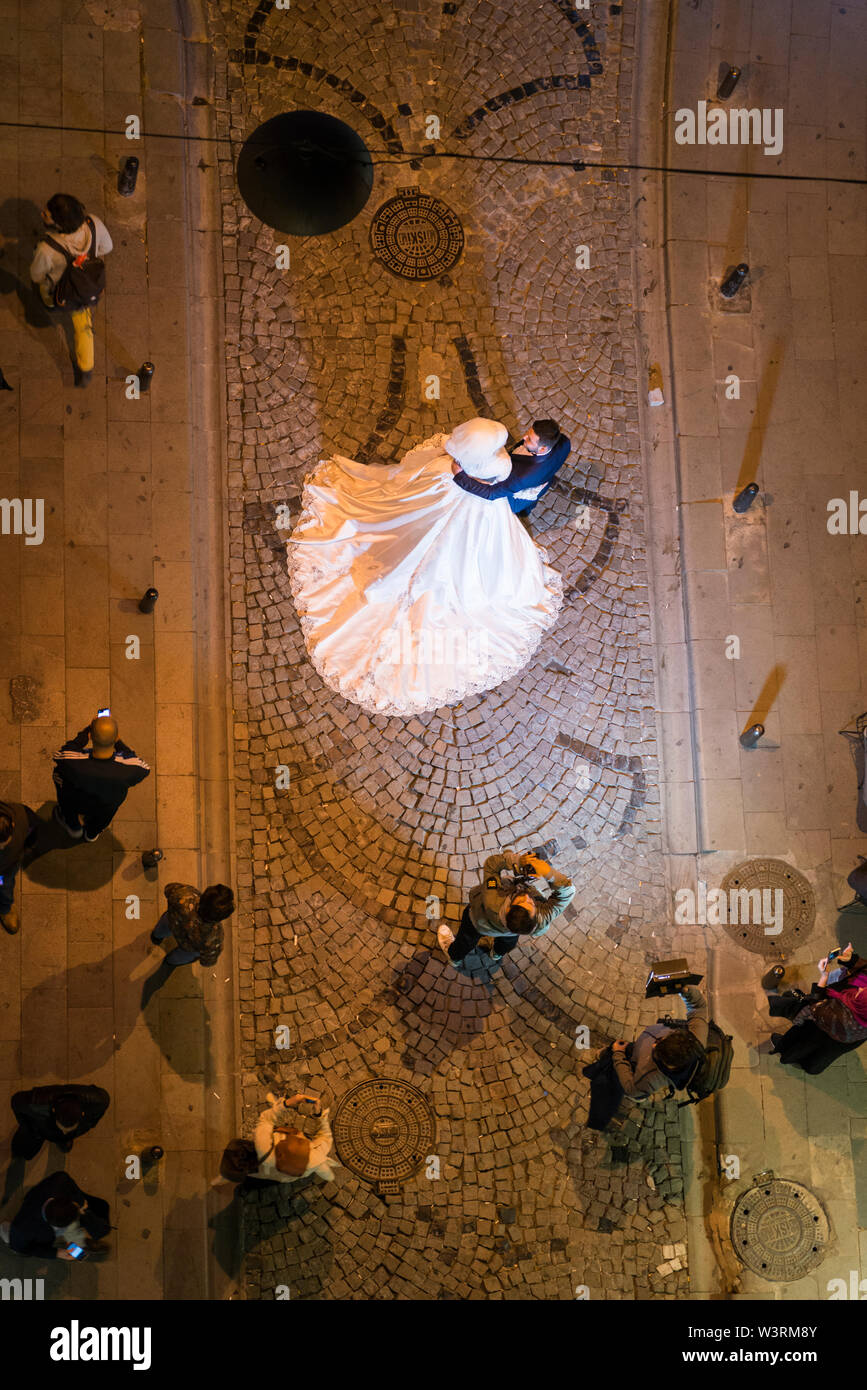 Topshot of a bride and groom posing as their photographer takes wedding photographs in a street by the Galata Tower at night. Istanbul, Turkey Stock Photo