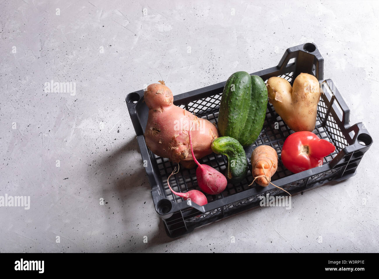 Ripe healthy ugly vegetables in plastic box on grey concrete background. Stock Photo