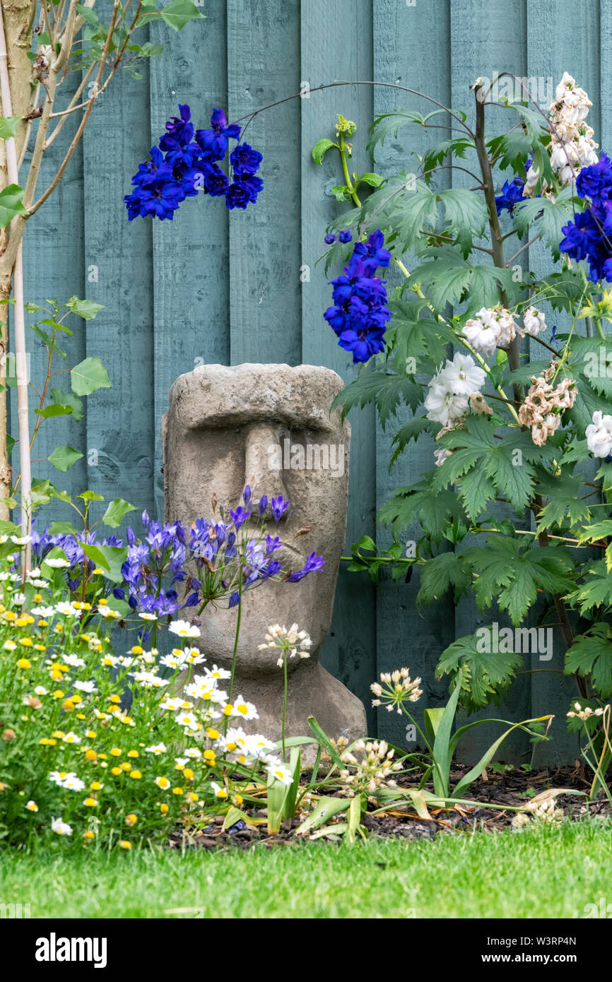 A reconstituted stone garden ornament in the form of one of the famous Easter Island heads sits nestled between flowers in a private garden Stock Photo