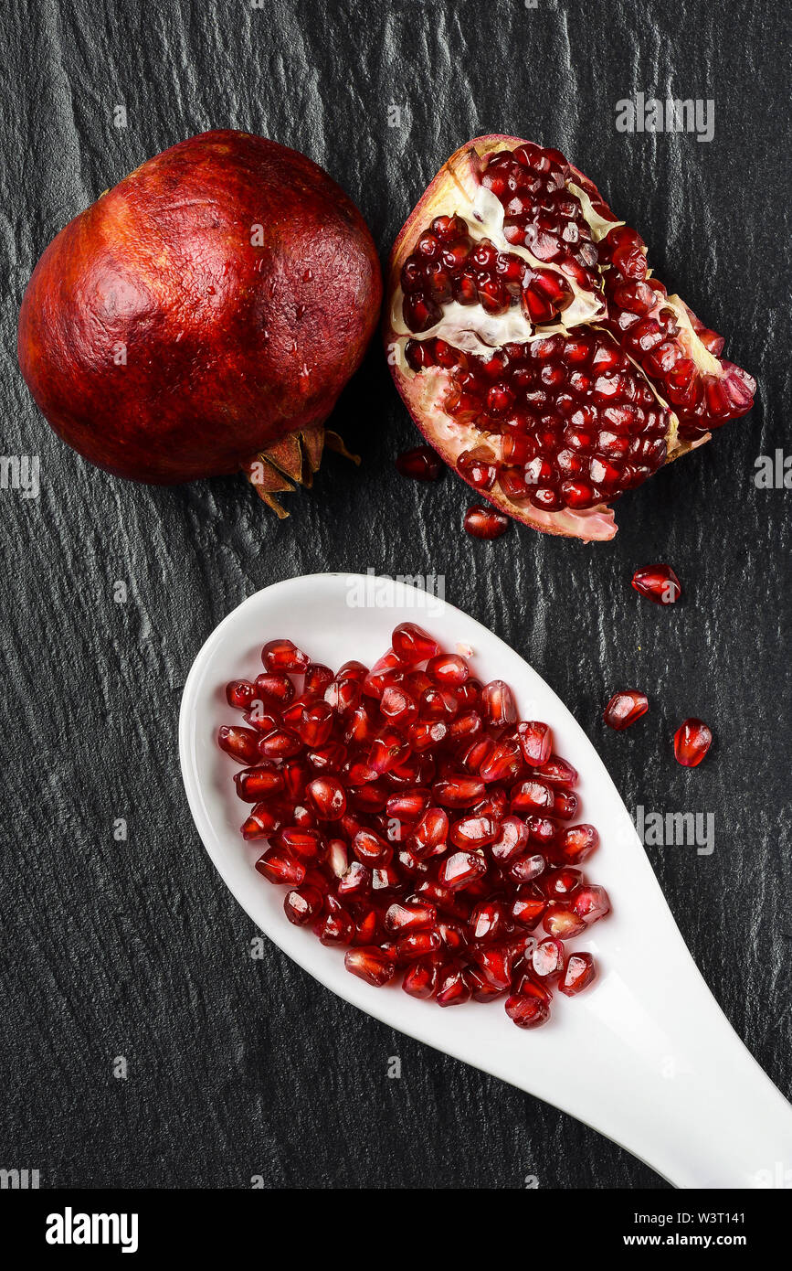 part of some pomegranates on a black slate stone and a spoon contains ...