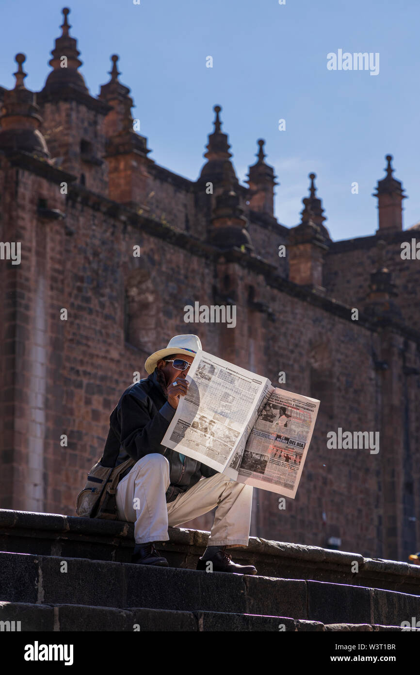 Man reading newspaper sat on the steps of the cathedral in the Plaza de Armas, Main square, backlit in Cusco, Peru, South America Stock Photo