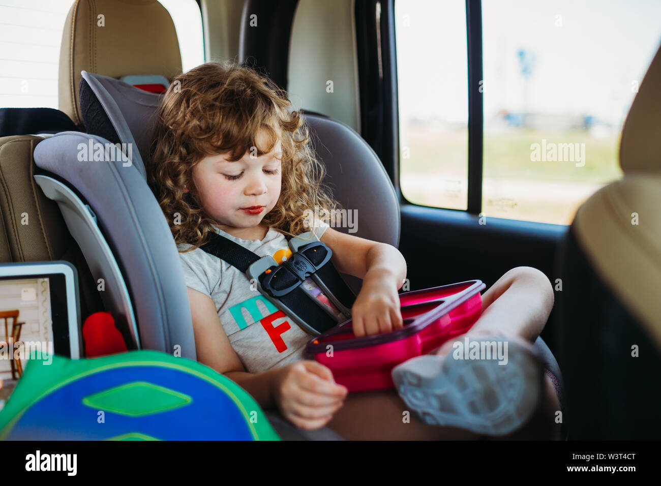 Young girl sitting in a car seat and eating lunch on a road trip Stock Photo