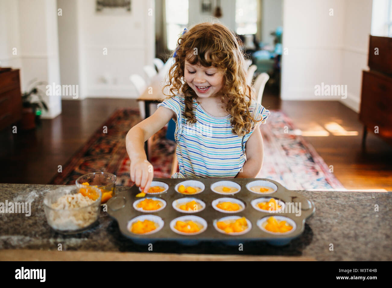 Young girl sitting in kitchen filling muffin tins with fresh peaches Stock Photo Alamy