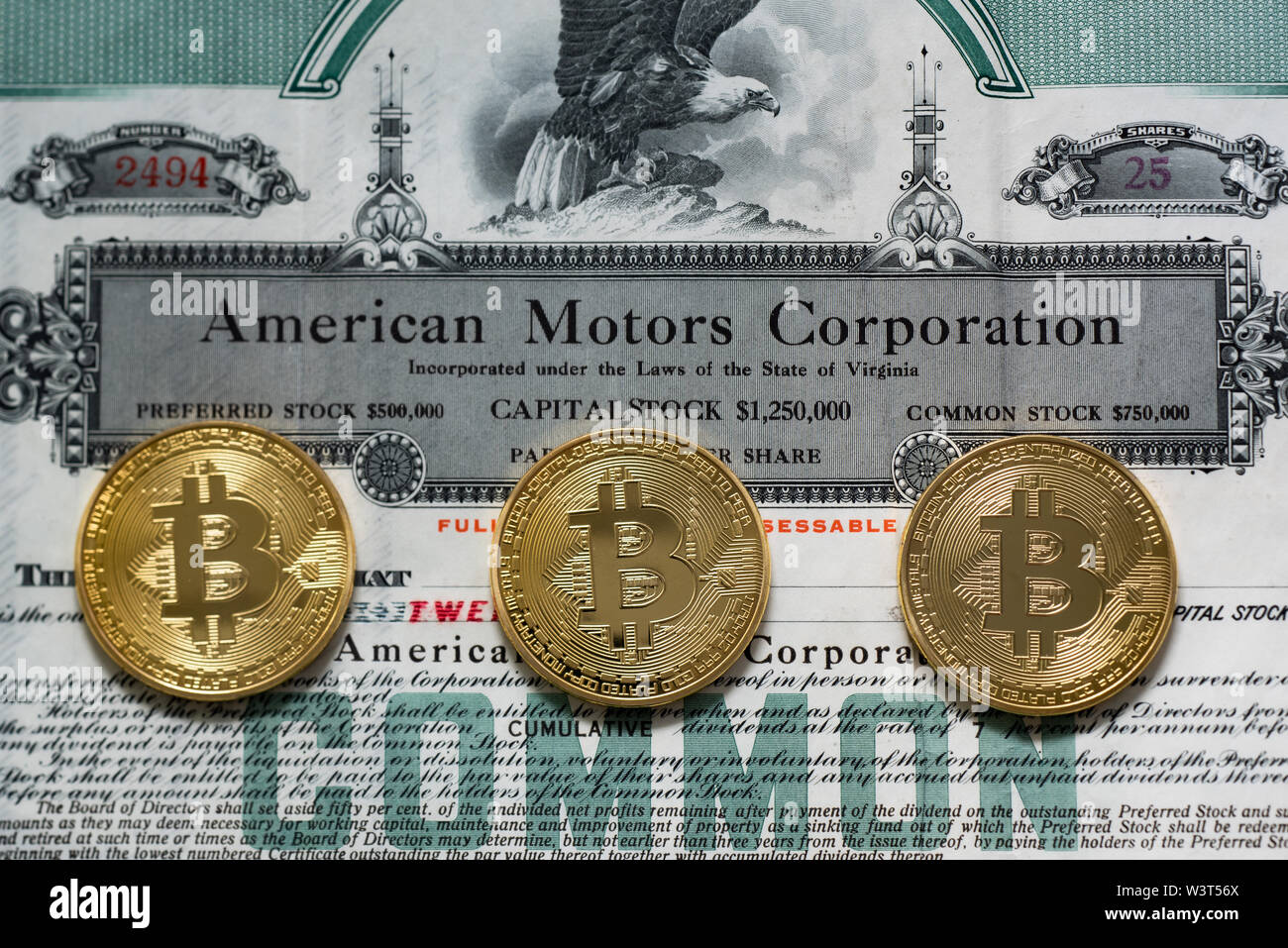 Three gold colored bitcoins on an old common stock certificate from American Motors Corporation, a comparison of value and risk in financial markets. Stock Photo