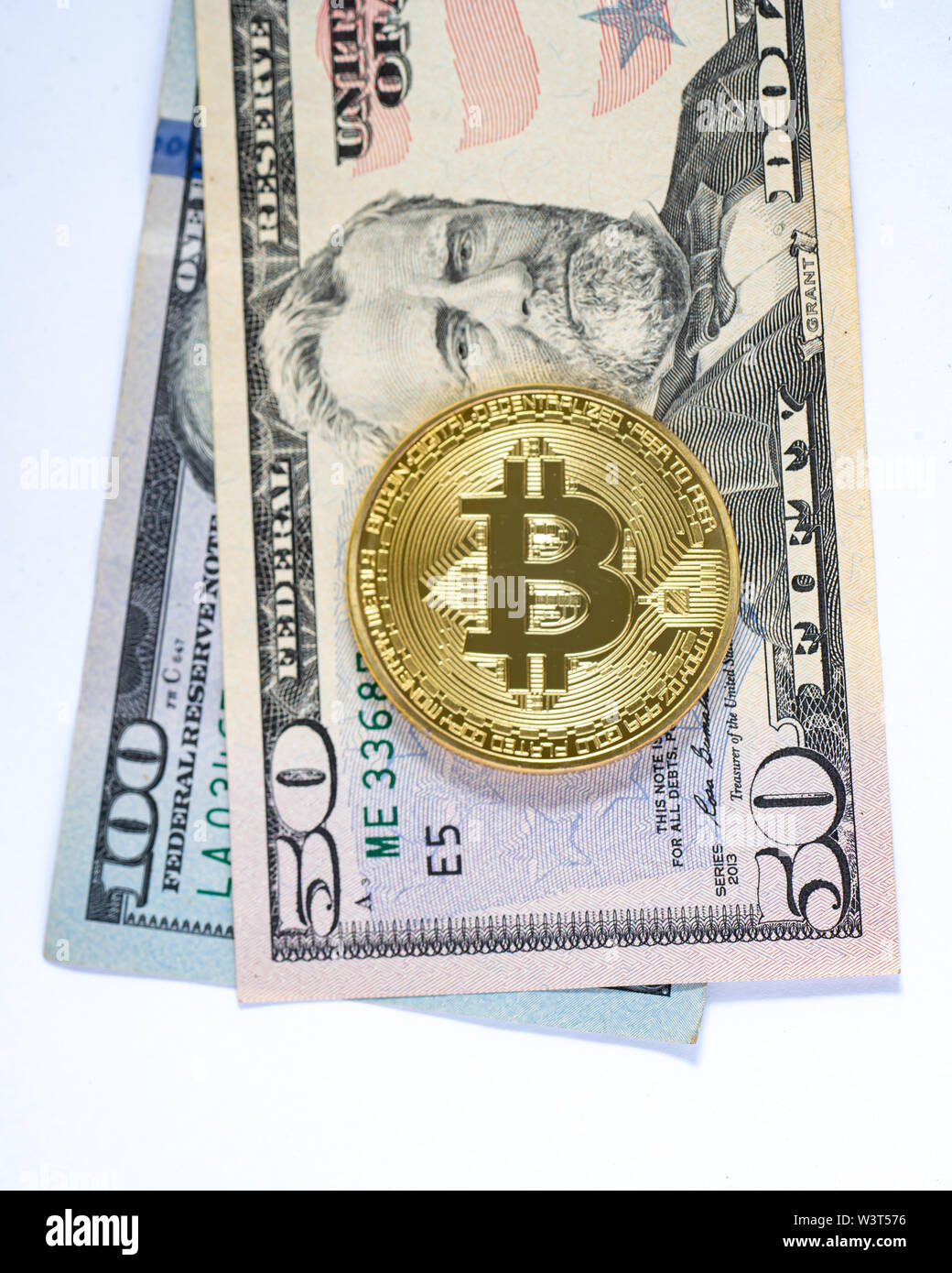 A gold colored bitcoin on $50 and $100 US currency bills isolated. Stock Photo