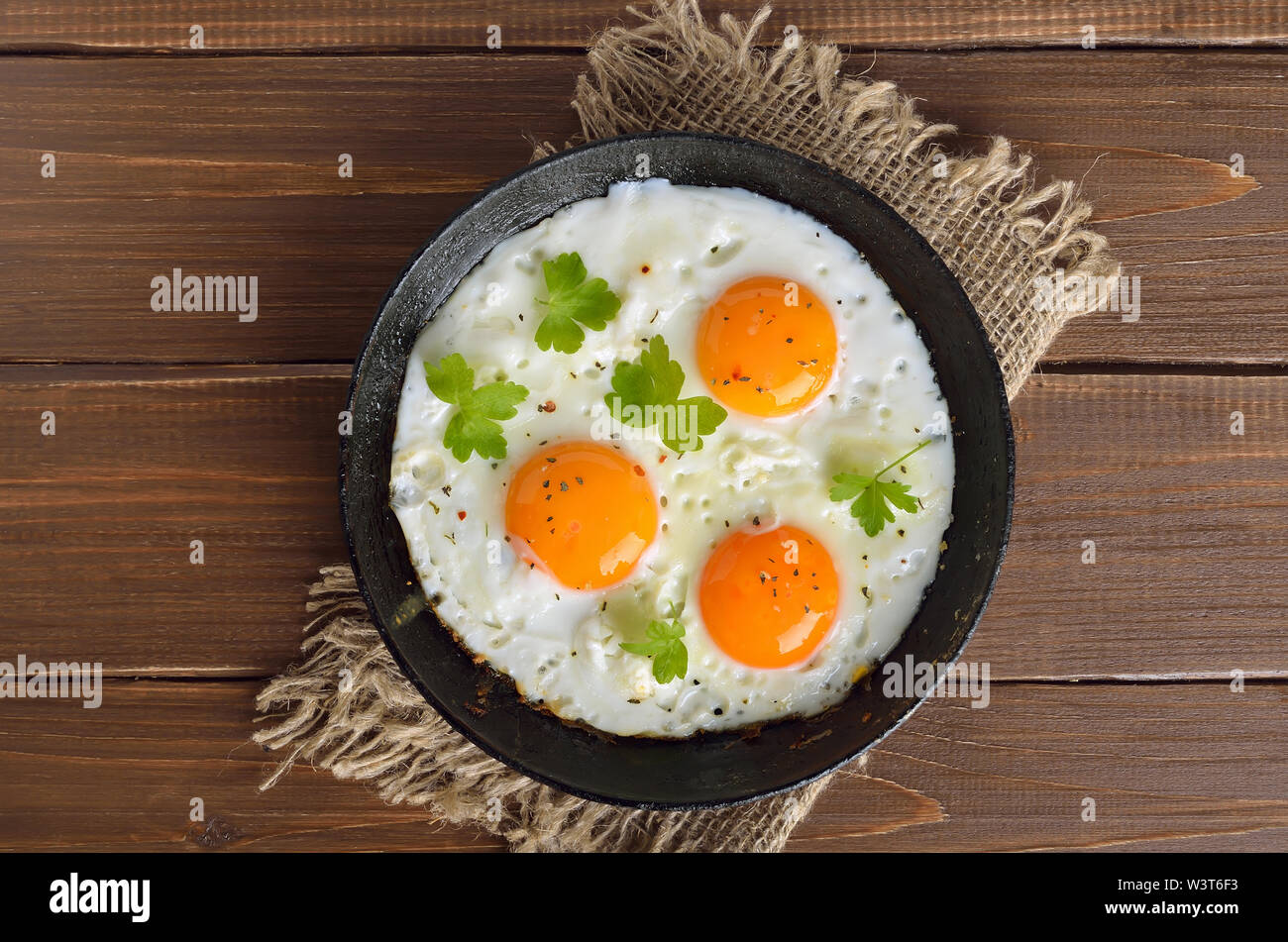 Appetizer fried eggs on frying pan on a wooden table. Top view, flat lay Stock Photo