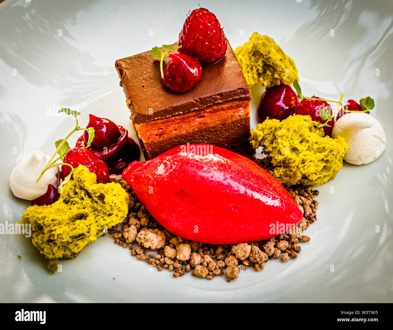 'Raspberry meets chocolate' is the name chef Frederik Desch gives this dessert at the restaurant of the Parkhotel Laudensack in Bad Kissingen, Germany: a chocolate tartlet with raspberry sorbet marinated in chocolate crumble and pistachio. Cherries, pistachio sponge and dollops of cream surround the composition. Stock Photo