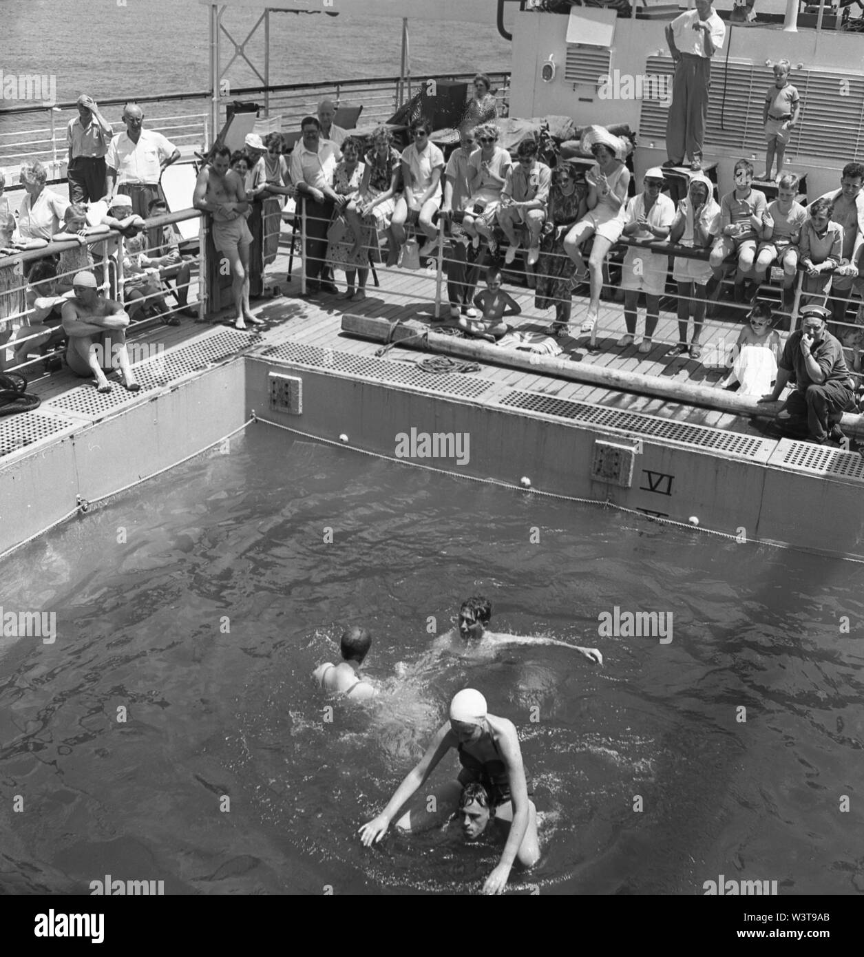 1960s, historical, out in the ocean, on board the cruise ship, Sagafjord, passengers standing watching other travellers enjoying the open-air swimming pool. Stock Photo