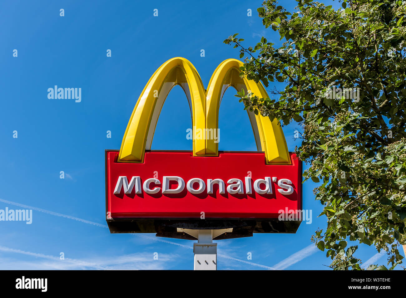 two golden bows, sign of MacDonald´s restaurant beside a green tree, Sweden, June 16, 2019 Stock Photo