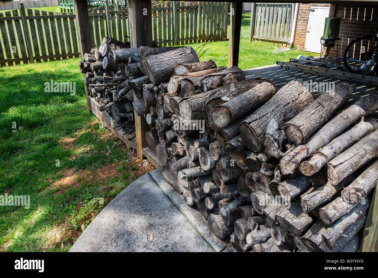 A rack of cut and stacked firewood stored in a yard under an overhang. USA. Stock Photo