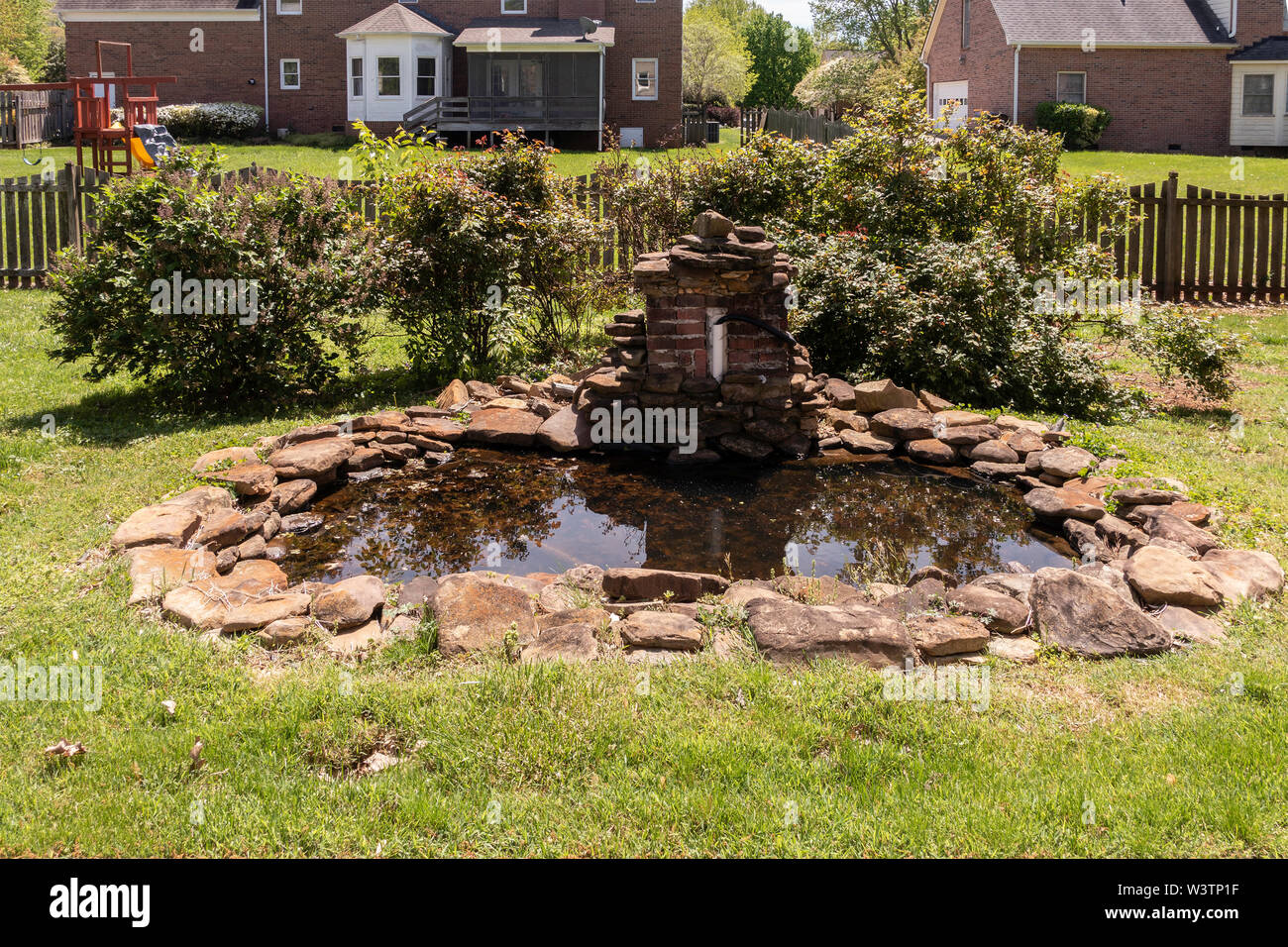 A koi pond surrounded by flagstones, stagnant and uncared for in a back yard. USA. Stock Photo