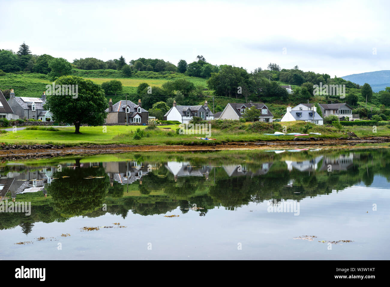 Early morning view of seafront houses reflected in the calm water of Loch Sween at fishing village of Tayvallich in Argyle and Bute, Scotland, UK Stock Photo