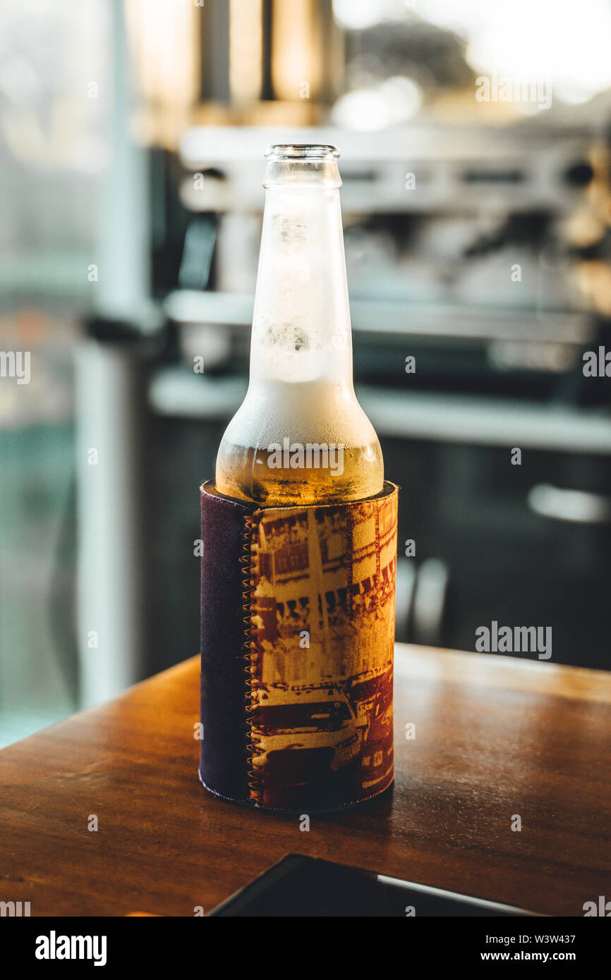 Beer in stubbie holder sits on wooden table of outdoor entertaining area. Stock Photo