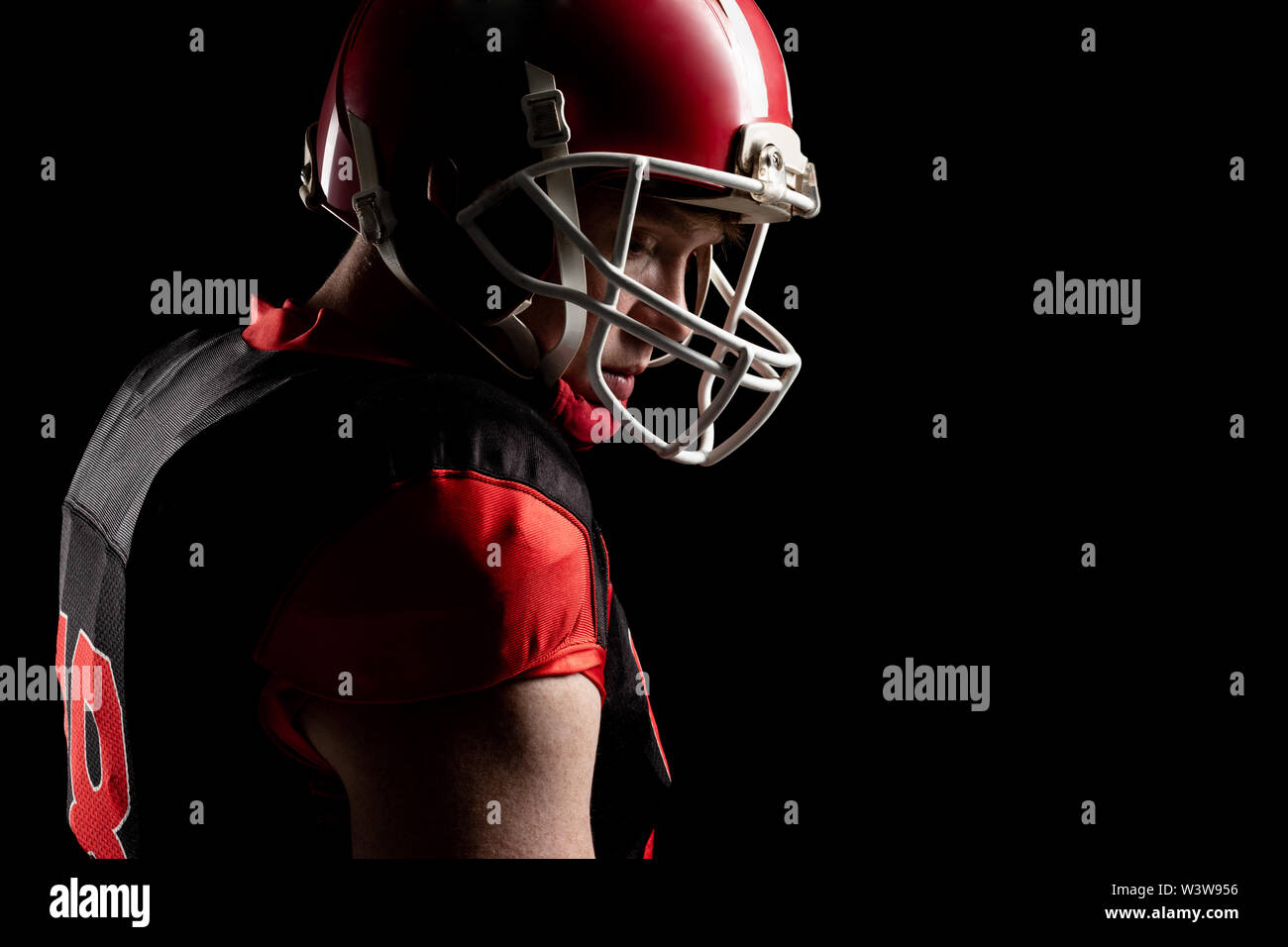 American football player in helmet standing against black background