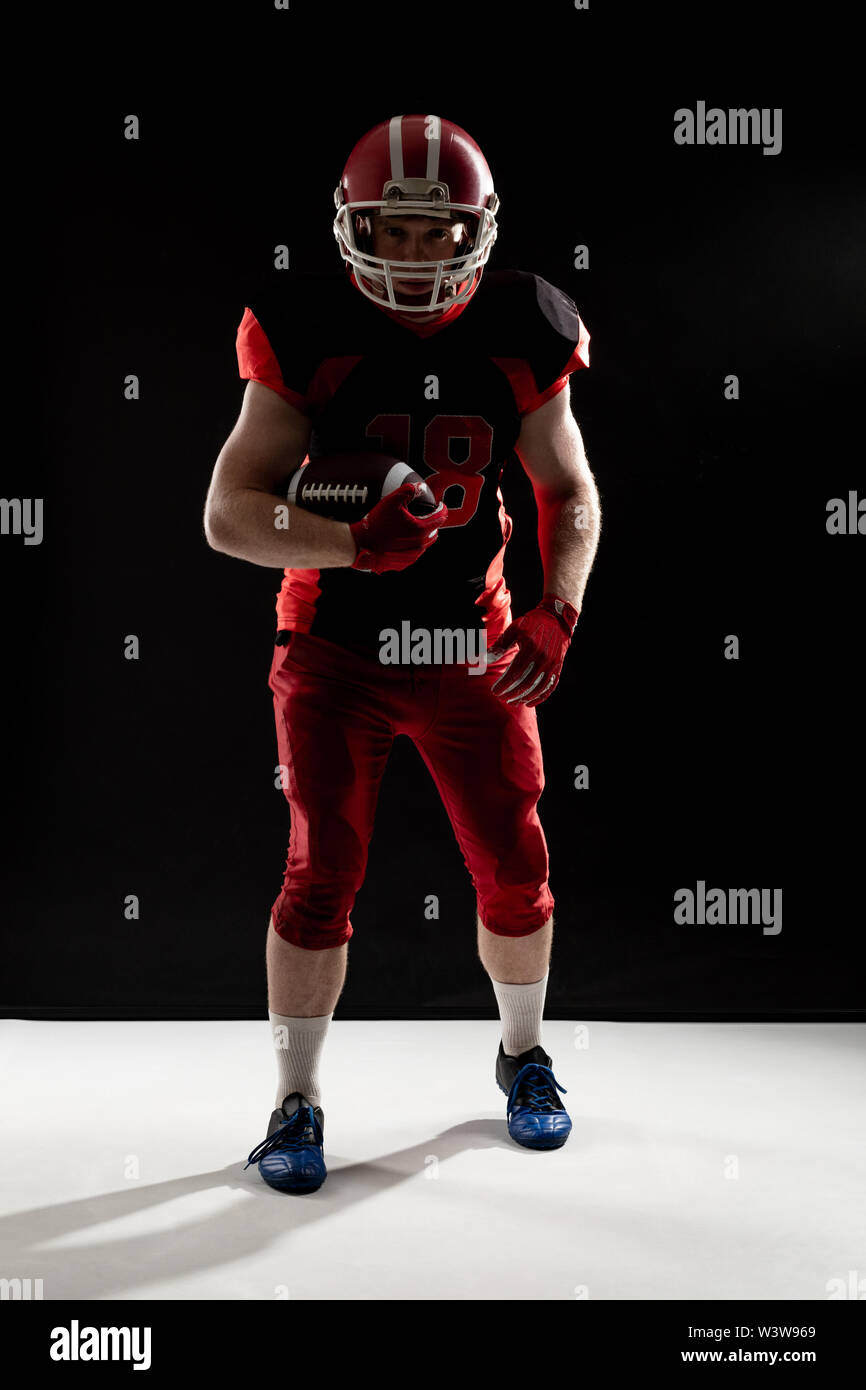 American football player in helmet taking position against black