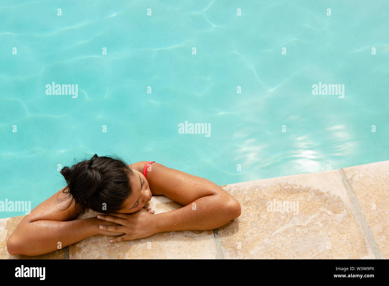Woman relaxing at the edge of swimming pool in the backyard at home ...