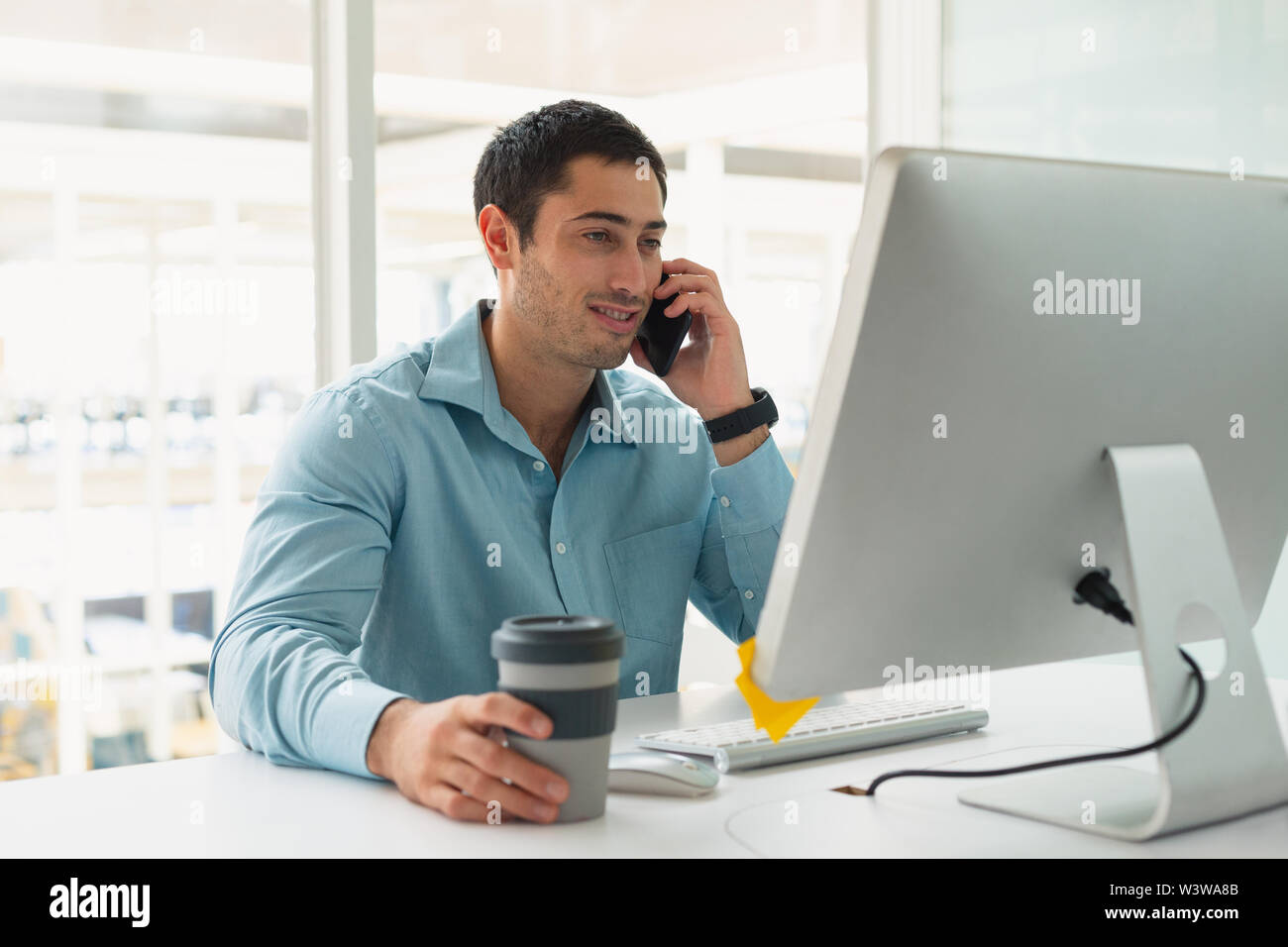 Male executive talking on mobile phone while working on computer at desk Stock Photo