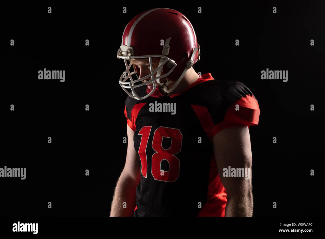 American football player in helmet standing against black background