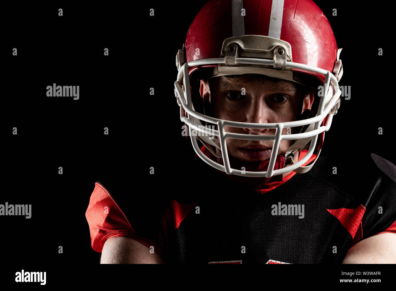 American football player in helmet standing against black background