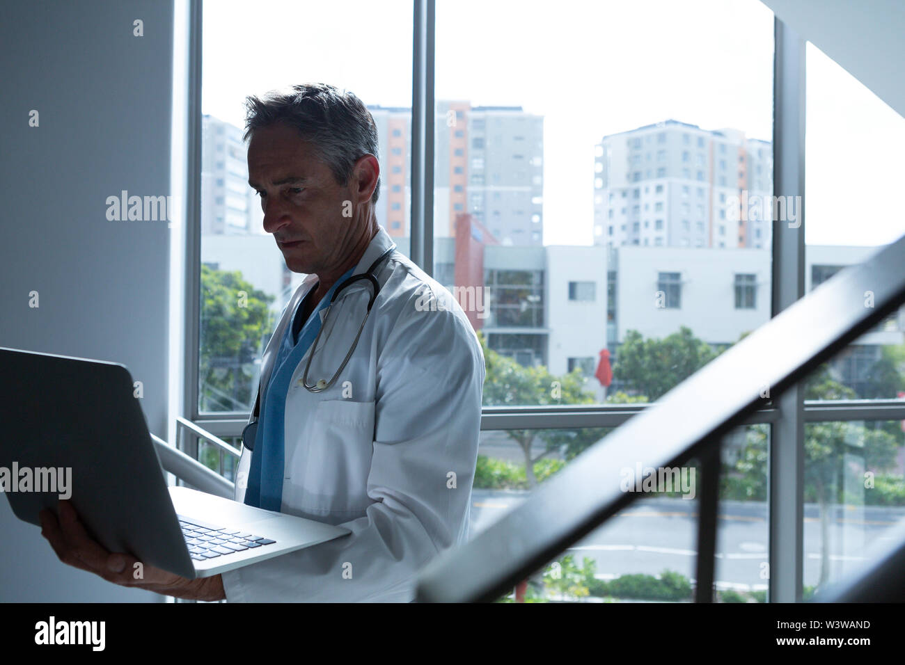 Male doctor using laptop while walking on stairs Stock Photo