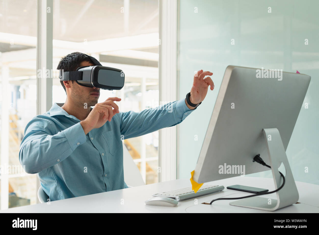 Male executive using virtual reality headset at desk Stock Photo