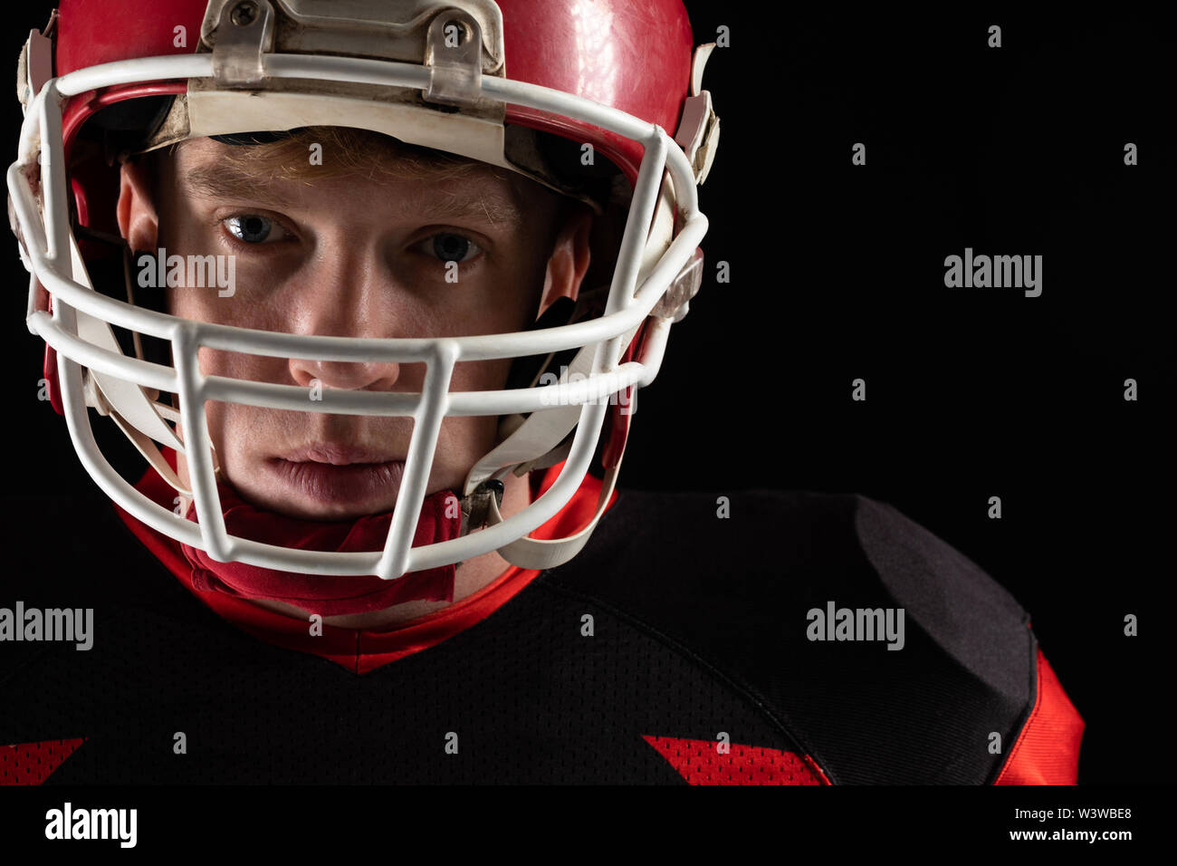 American football player in helmet standing against black background