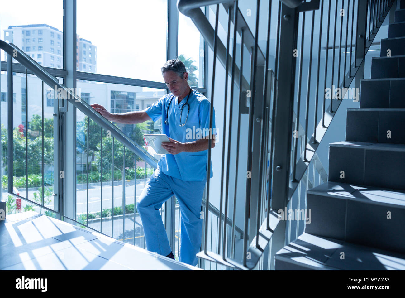 Male doctor using digital tablet while going upstairs Stock Photo