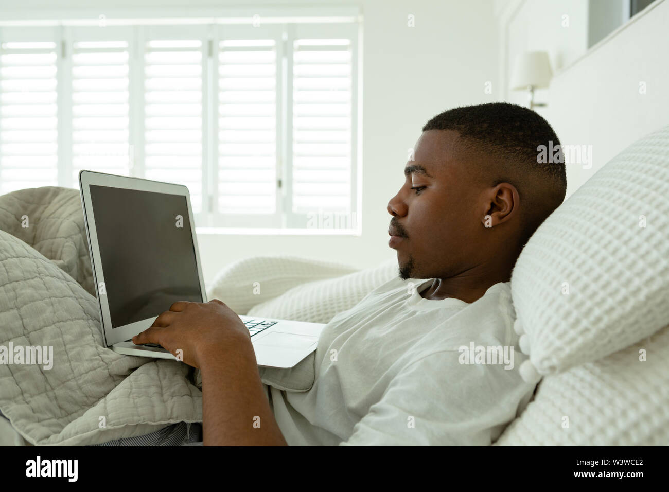 Man using laptop while lying on bed in bedroom at comfortable home Stock Photo