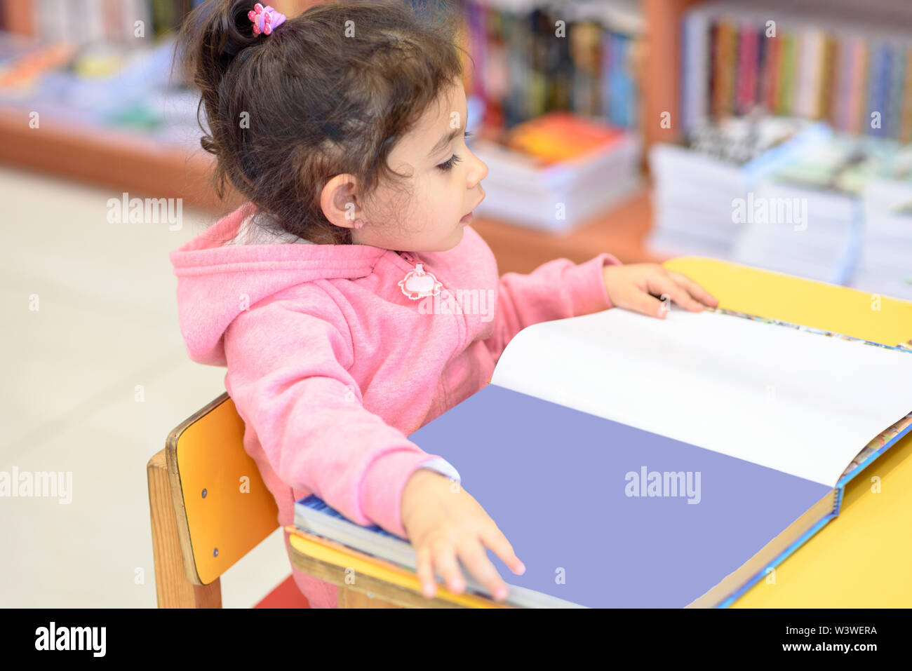 Little Girl Indoors In Front Of Books. Cute Young Toddler Sitting On A