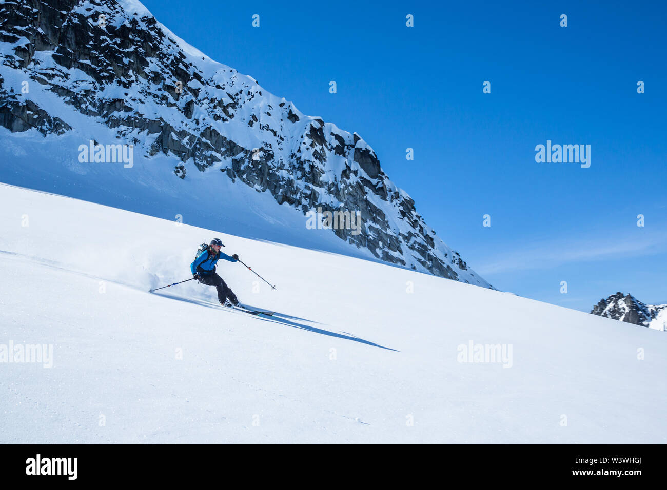 Soft snow on a bluebird day, a skier rips downhill in teh backcountry of Alaska's Talkeetna Mountains. Stock Photo