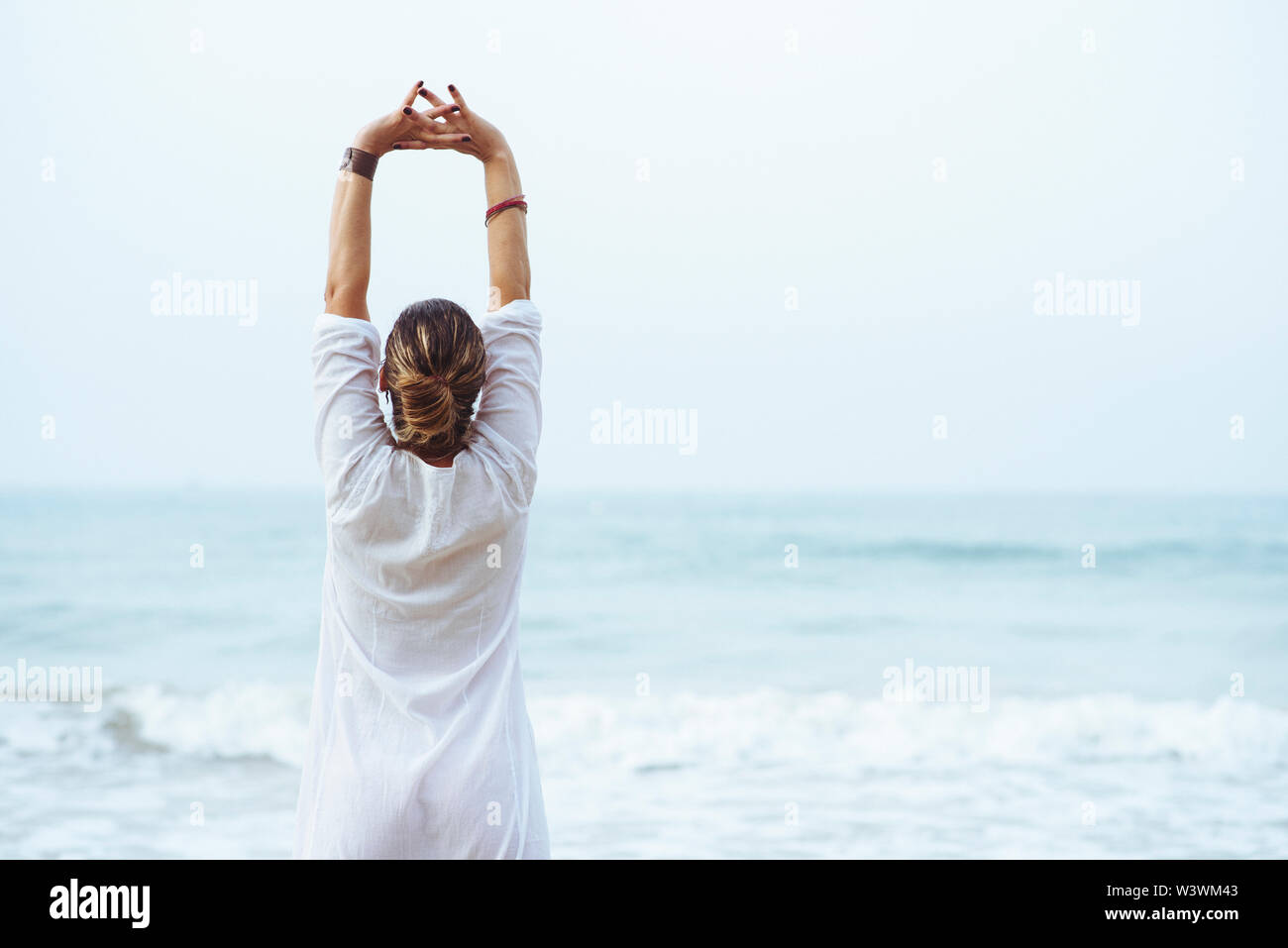 Woman with her back and white dress doing stretching on the beach. Stock Photo