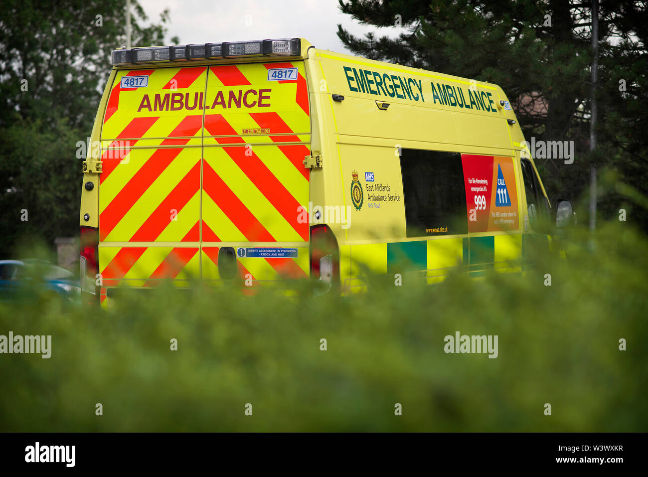 Emergency Ambulance sits outside an NHS, GP Surgery, among some greenery . Stock Photo