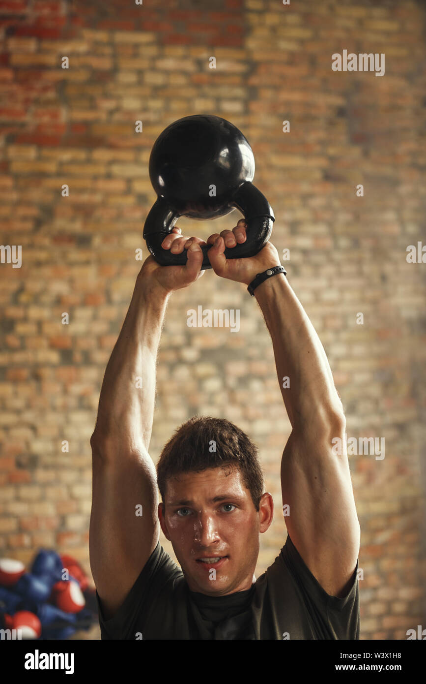 Strong and handsome man holding big black dumbbell under his head while exercising at gym. Weight exercises. Bodybuilding concept. Workout. Stock Photo