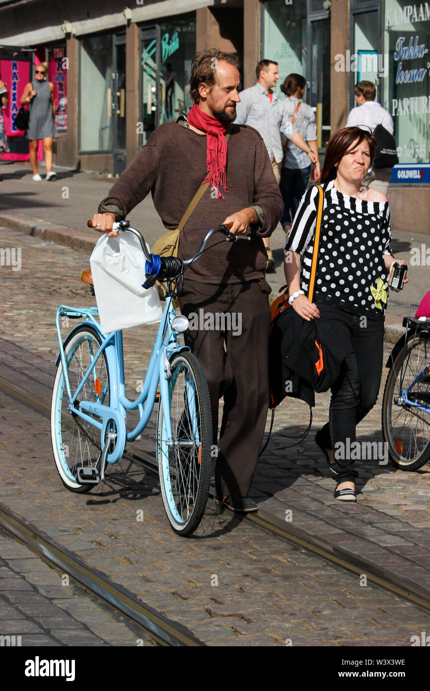 Man with a red scarf walking a bike by tramway tracks down Porthaniankatu in Helsinki, Finland Stock Photo