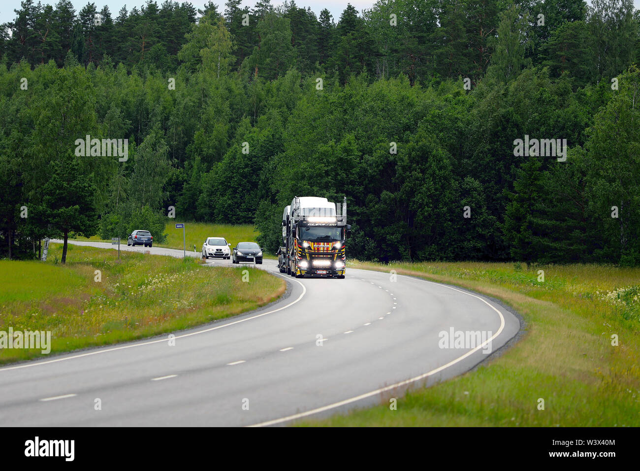 Salo, Finland - June 29, 2019: Bright headlights of unique vehicle carrier Scania R650 of Kuljetus J. Kivi light up the rural highway on day of summer Stock Photo