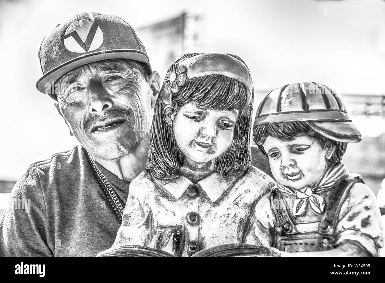A black and white image of a poor, middle aged man, trying to sell a statue of two young children, at the USA/Mexico border crossing. Stock Photo