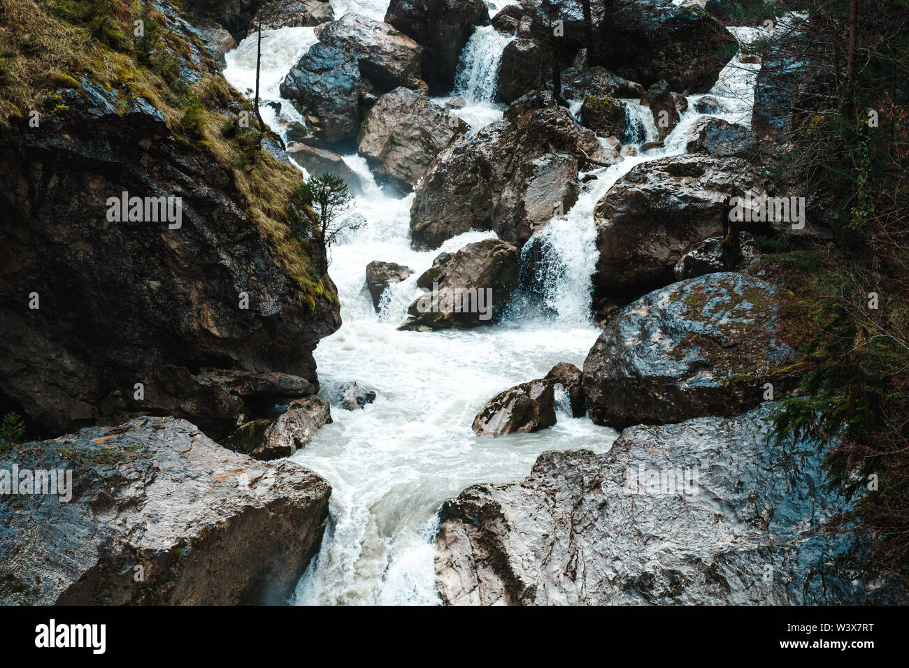 Small cliffy mountain spring waterfall in Abkhazia. Craggy ridge cliff with water bursts. Rocky mountains and waterfall rounded by trees. Stock Photo