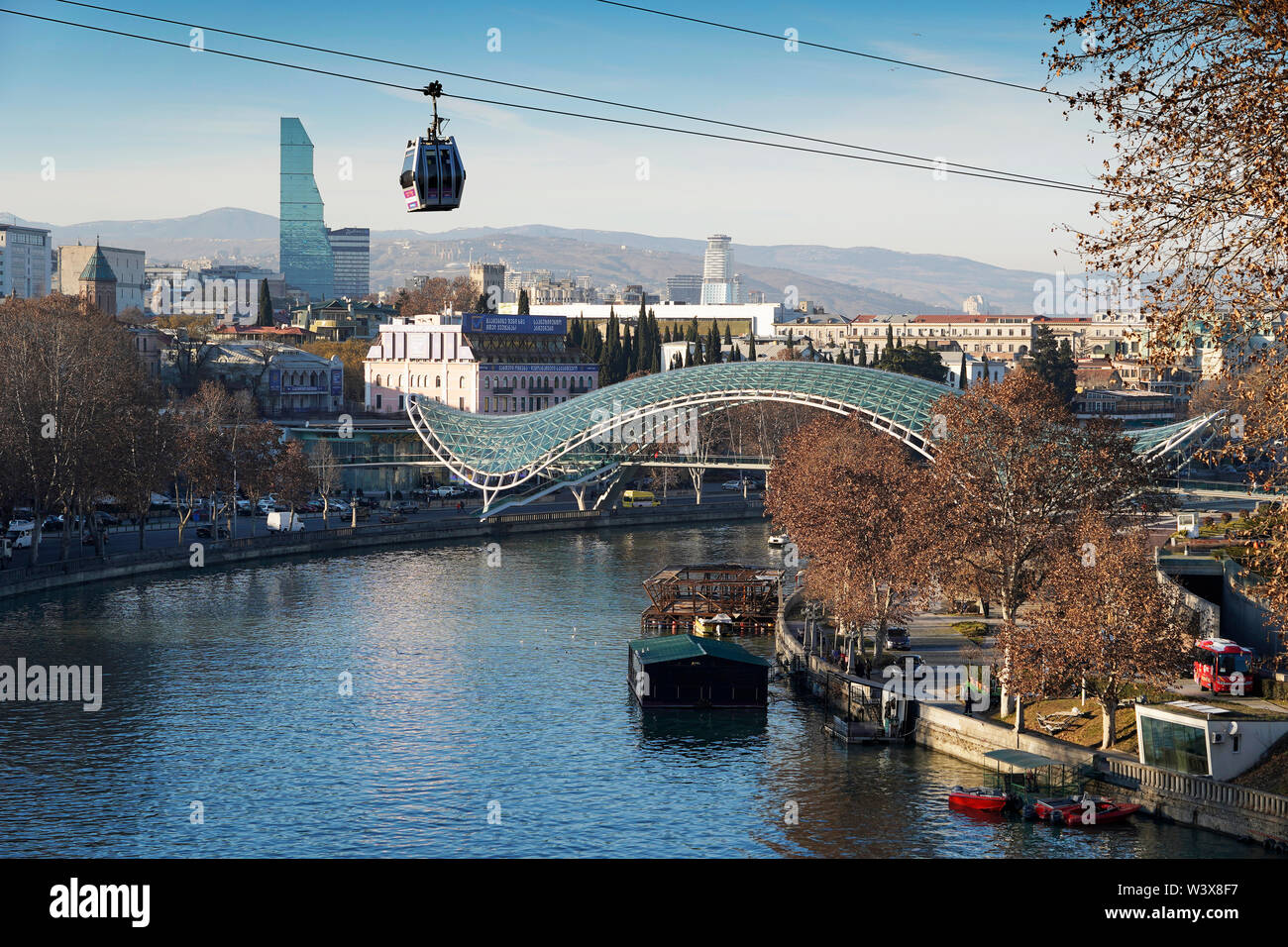 A cable car gondola hovers over the Mtkvari river. In the background: The Bridge of Peace from Michele De Lucchi. Downtown Tbilisi, Georgia, Caucasia Stock Photo