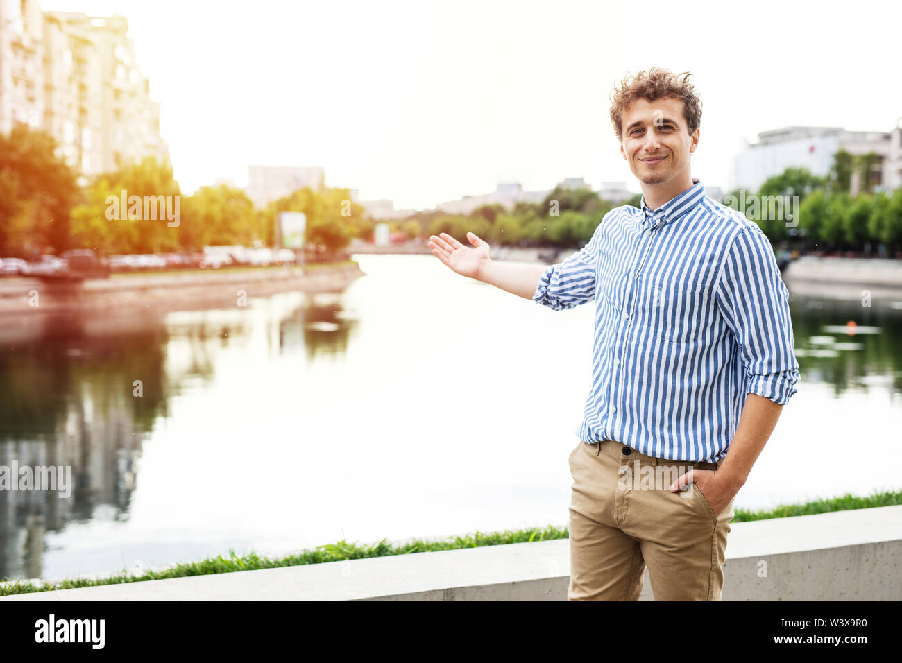 young man smart casual dressed looking with confidence to camera presenting a european city with a river behind Stock Photo