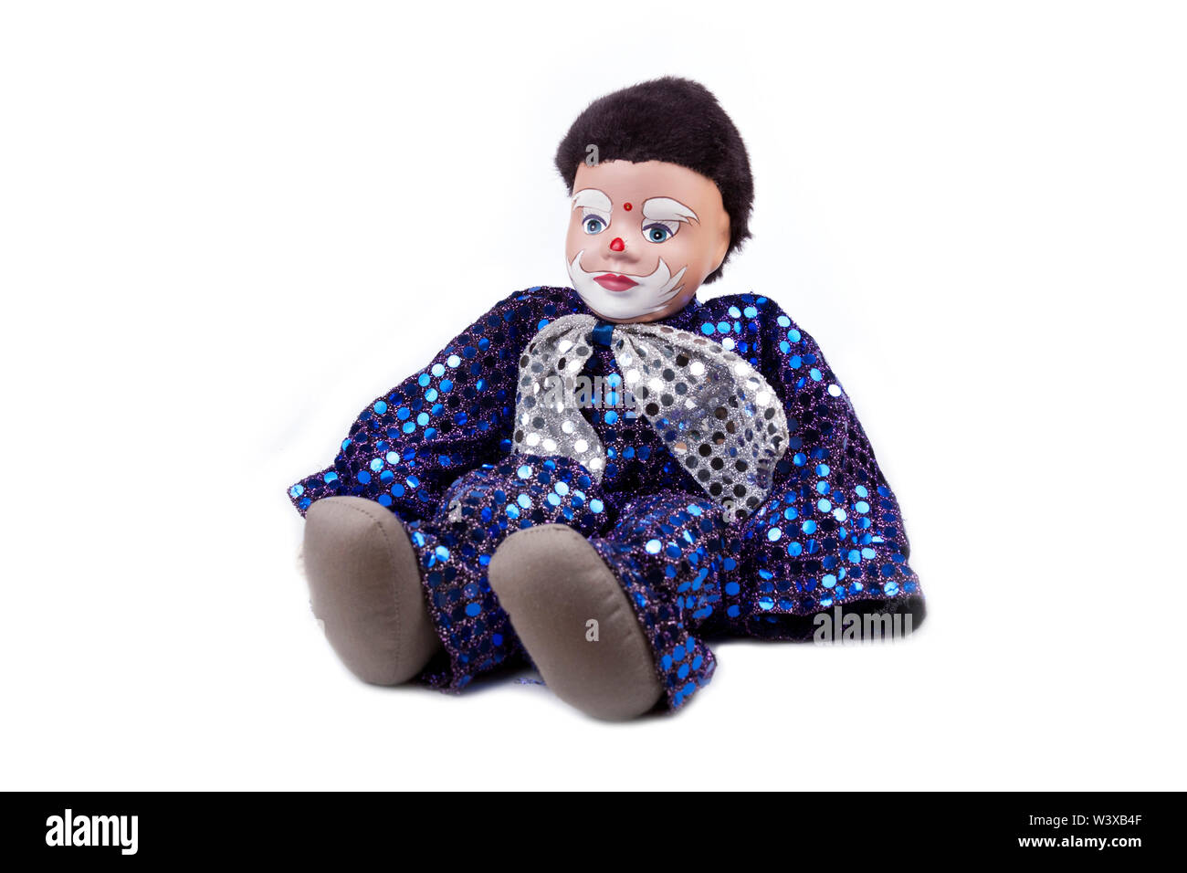 A little blue black haired boy clown like doll with shiny sequins and a bow on the neck, sitting pose. Isolated on white, detailed puppet Stock Photo