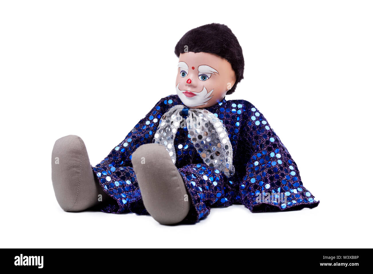 A small blue black haired boy clown like doll with shiny sequins and a bow on the neck, sitting pose. Isolated on white, detailed puppet Stock Photo