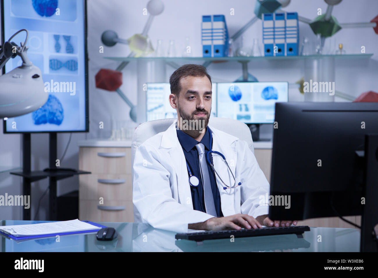 Portrait of young doctor in white coat working in his hospital office. Hospital technology. Stock Photo